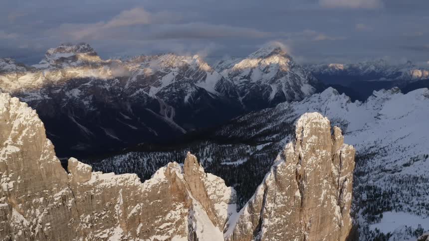 Snow covers sections of a mountain range and the ground on the forest below