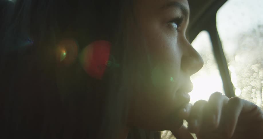 Woman sitting in the back seat of the car looks out the window while it rains