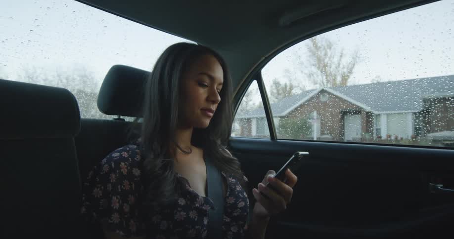 Young female passenger scrolling on cell phone in back seat of car