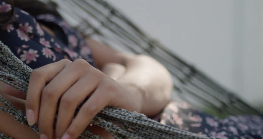 Woman with a dress lies in a net hammock in the backyard