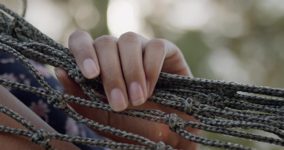 A woman laying in a hammock lays her hand over the rope