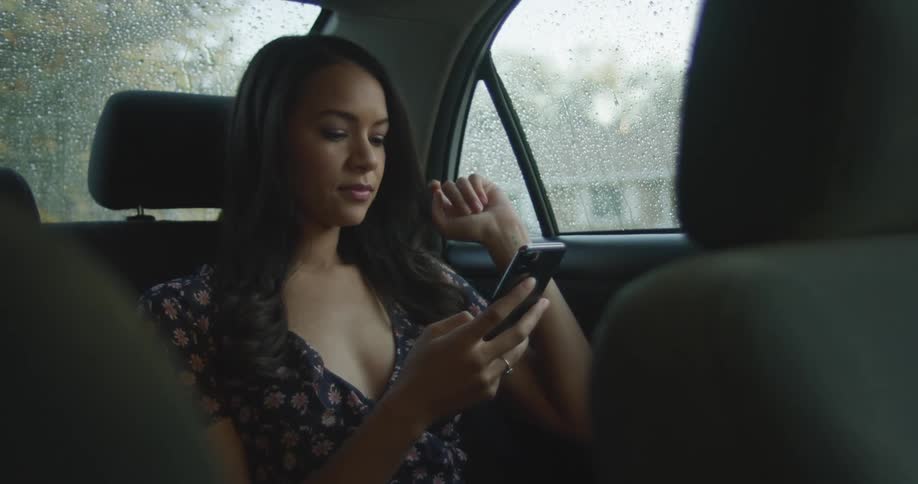 A teenage girl sits in the back seat of a car and scrolls through her cell phone