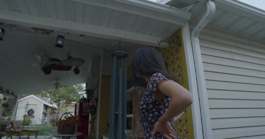 A young woman stands by a home carport looking around as if trying to find something or someone
