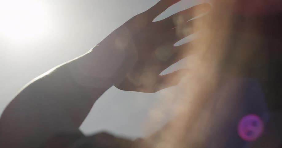 A woman with her hand towards the sky with a house the sun the sky and clouds in the background