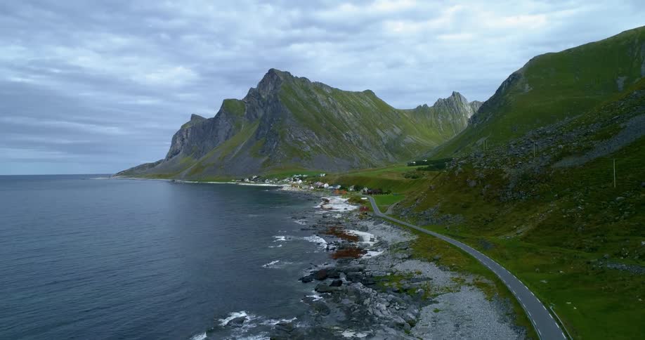 A narrow road between the ocean and a mountain covered in greenery on a cloudy day