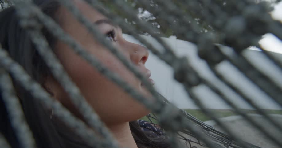 Brunette woman with dark straight hair and a dress lies in a net hammock in the yard