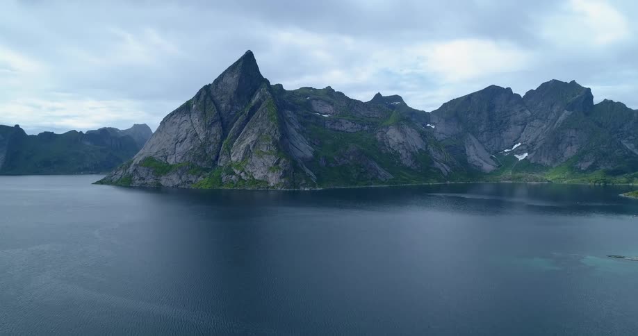 An aerial view of the ocean with mountains and an overcast sky