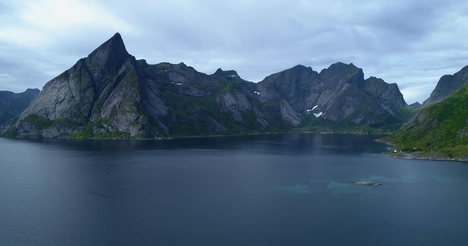 Rippling water borders rocky and vegetation covered mountains on cloudy day