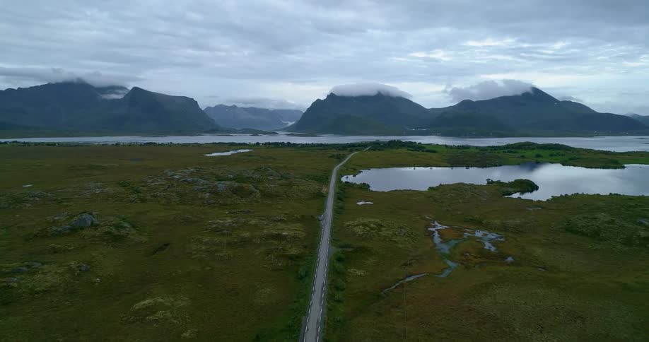An aerial view of a road through remote area with mountains and a body of water