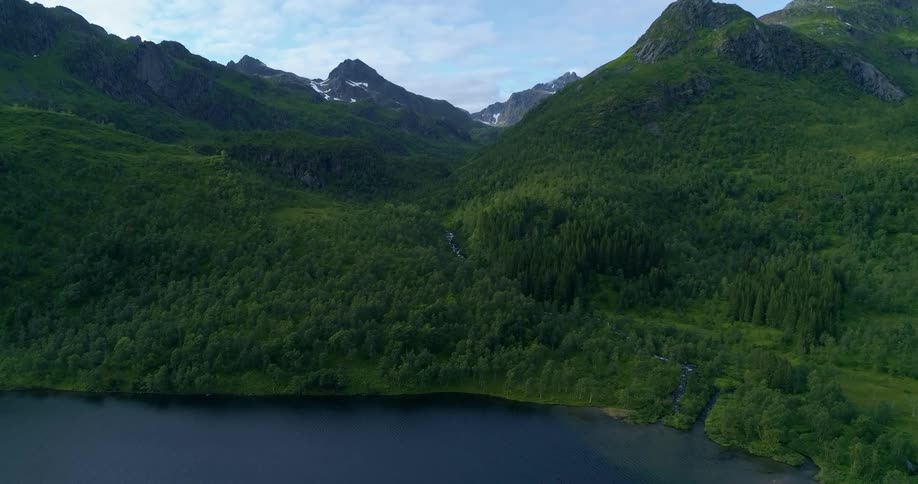 Mountain forest with a lake and summit peaks high in the cloudy sky