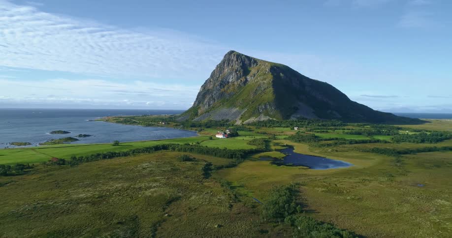 Small home in a rural location in front of a single large mountain next to a small lake and the ocean