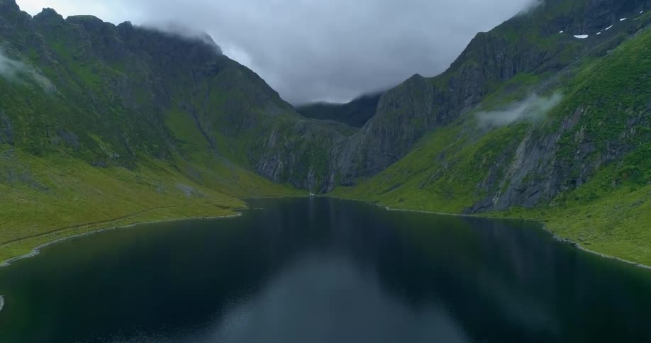 Aerial view of a river in between large grass covered mountains on a cloudy day