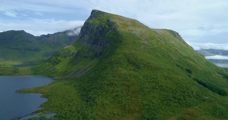 Aerial view of the green peak of a mountain in a mountain range next to lakes