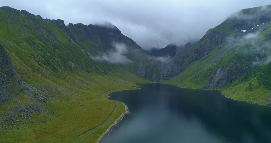 Calm waters of a lake in the valley between the cloud covered peaks of a mountain range