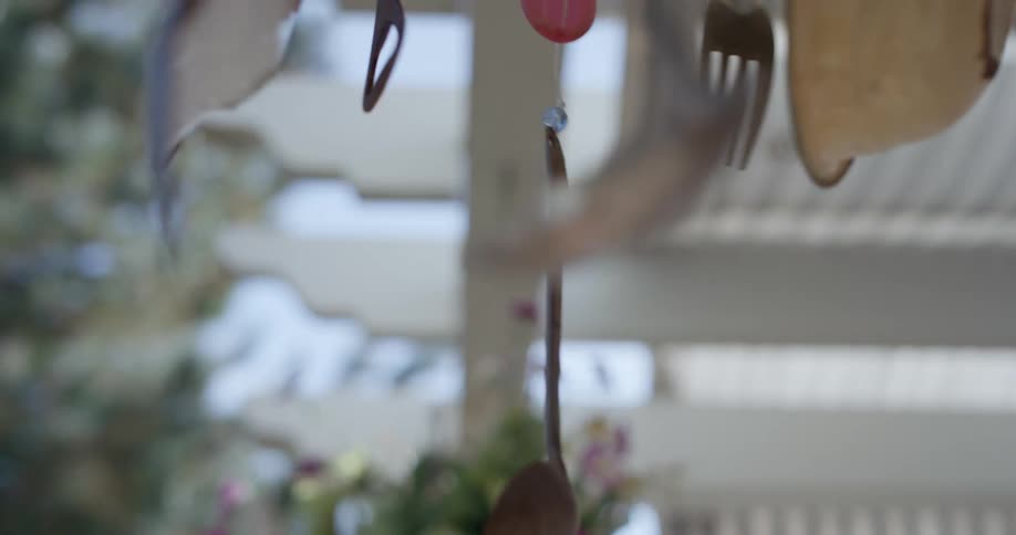 A mobile made of cutlery and bowls hangs on a porch