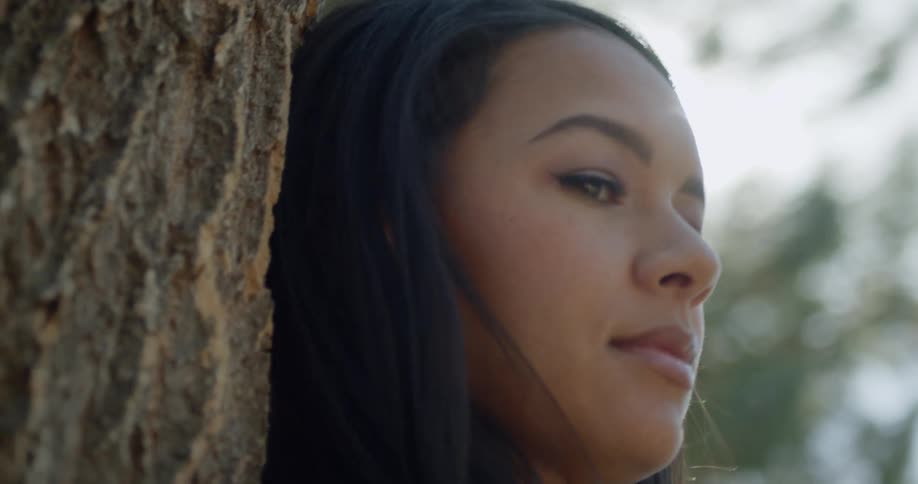 Close up of the face of a woman reclined on the trunk of a tree
