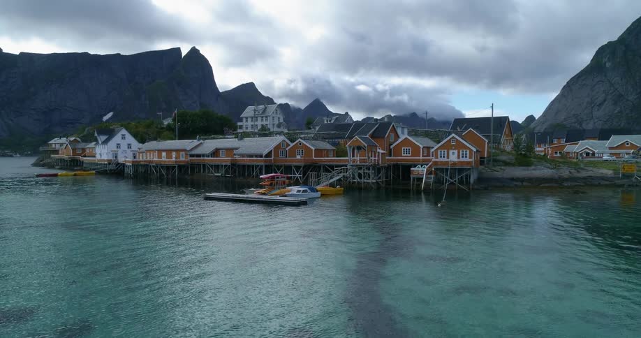 Red and white homes next to the ocean on a dock surrounded by large ocean side mountains at day time