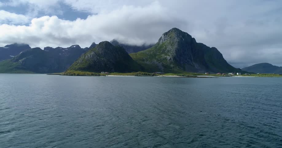 An ocean coastline contains small mountains covered in vegetation