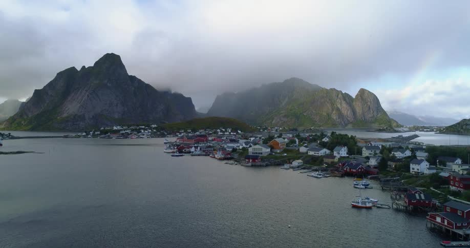 An aerial view of water with a town on the coastline and mountains with mist and rain
