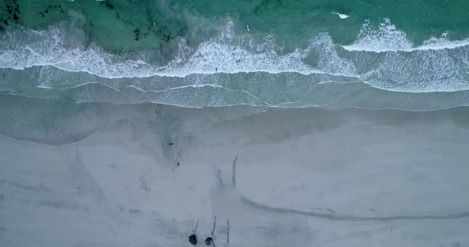 Aerial view of ocean waves breaking against the white sand beach