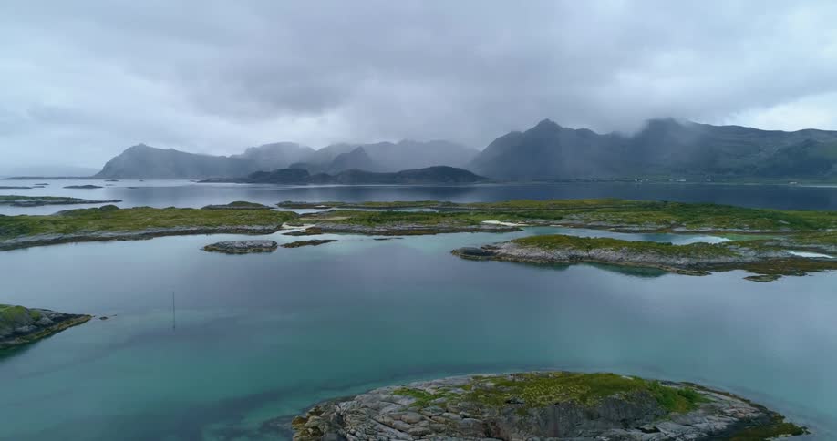Small rocky islands covered with moss and grass in front of mountains covered in fog