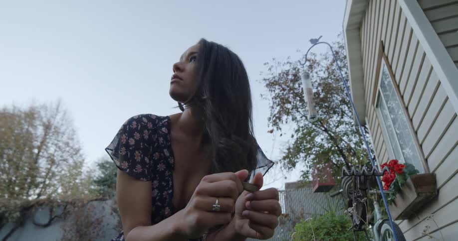 A young woman kneeling in the yard of a house examines a stone before looking around at her surroundings