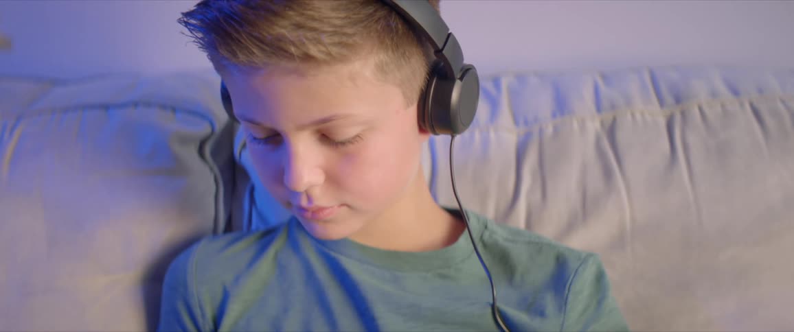 A boy sits on a couch with a tablet wearing headphones