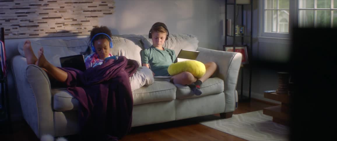 Two children a boy and girl sit on a couch together watching tablets