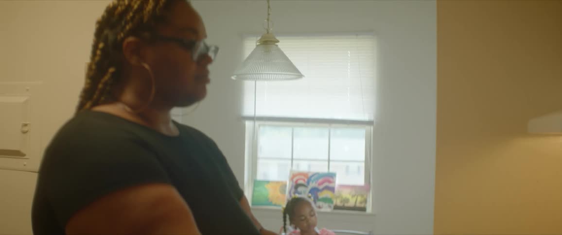 A woman sits and types while a girl paints in the background indoors