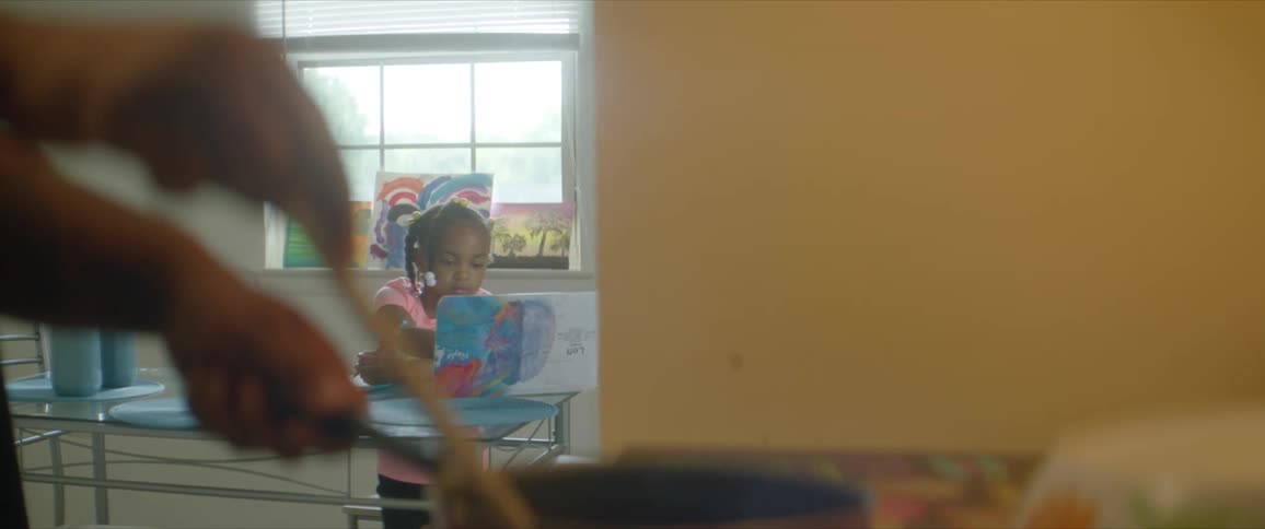 Little girl at a table in a dining room painting on a small canvas on a table