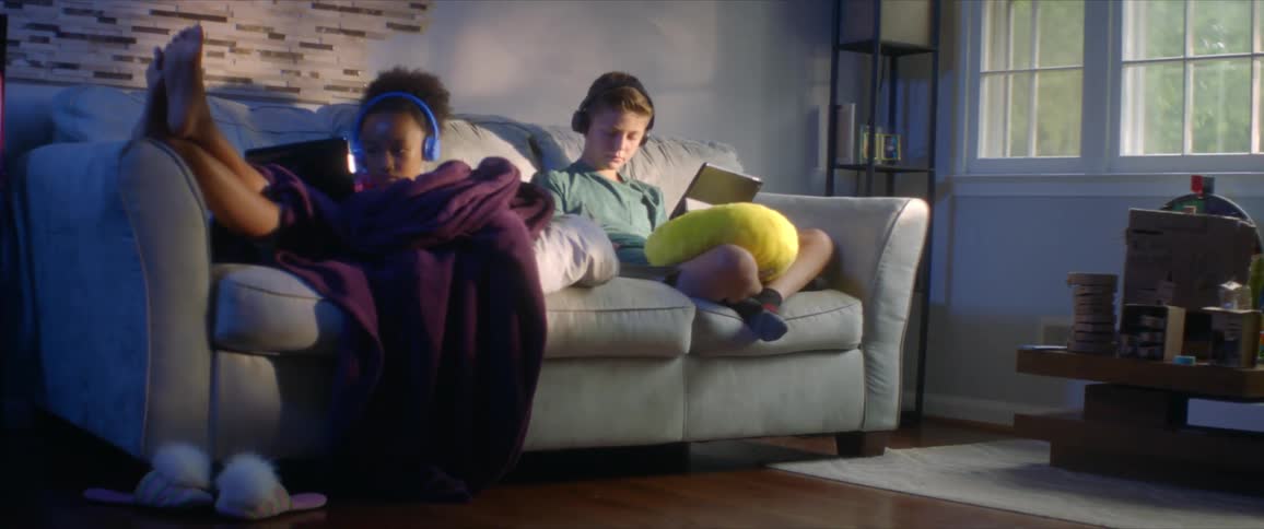 Young boy and girl sitting on a couch in a living room doing their homework on tablets