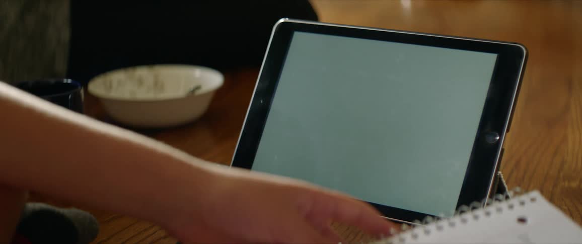 Boy sits on the ground holds a notebook next to a tablet with white screen