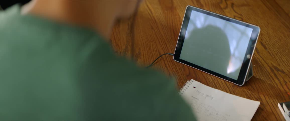 A person sits at a table in front of a tablet holding a piece of paper