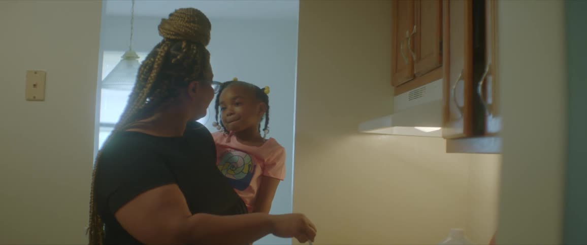 A woman holds a young girl on her hip while stirring a pot on the stove