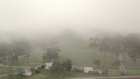 Aerial view of low clouds hanging over the rows of white tombstones in the cemetery