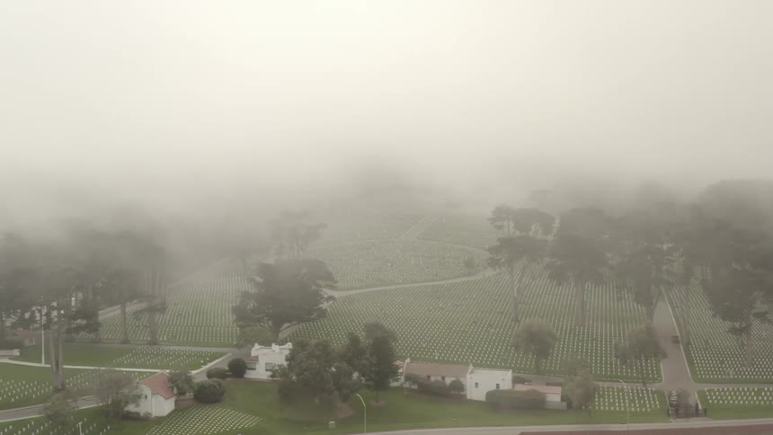 Aerial view of low clouds hanging over the rows of white tombstones in the cemetery