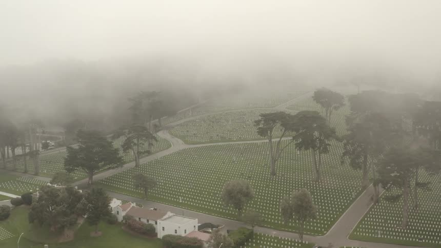 Aerial view of the rows of white headstones on the green grass of a graveyard under the clouds