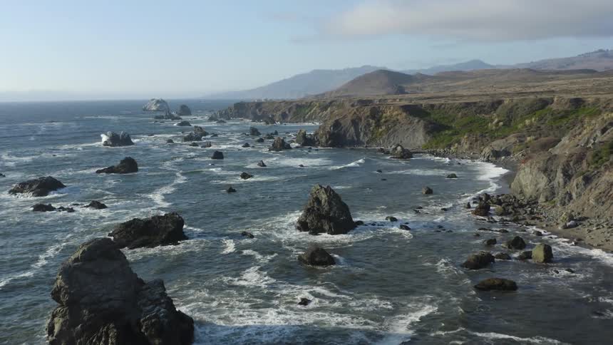 Waves roll in on rocky a coastline with mountains on the horizon