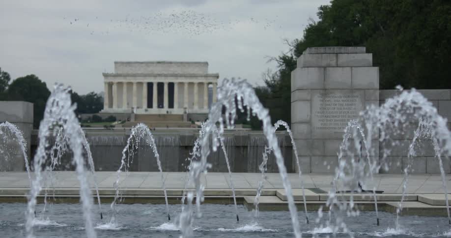 A water fountain with a building trees the sky and clouds in the background
