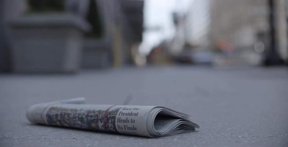 A newspaper lying on a city street with construction workers and cars driving