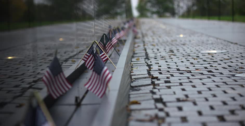 Flags on a monument for fallen soldiers with lights a road and trees in the background