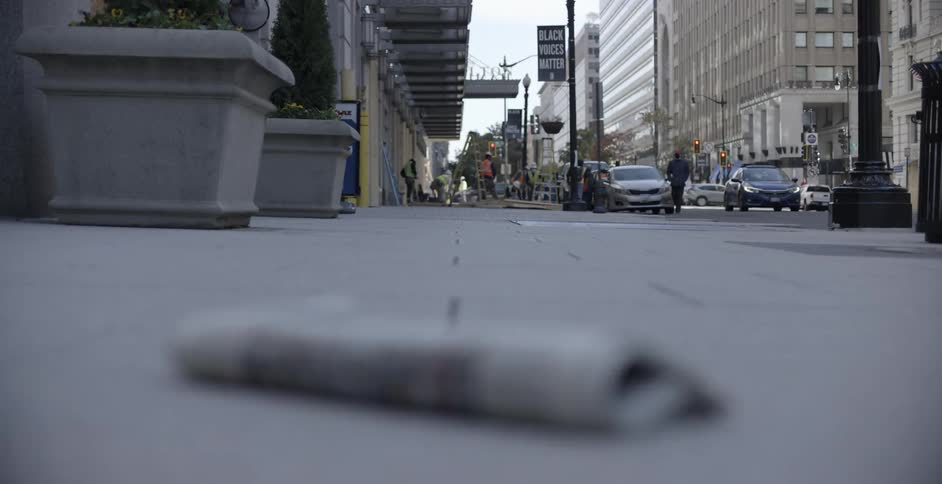 A newspaper of election results lying on a city street with cars driving people walking and construction workers