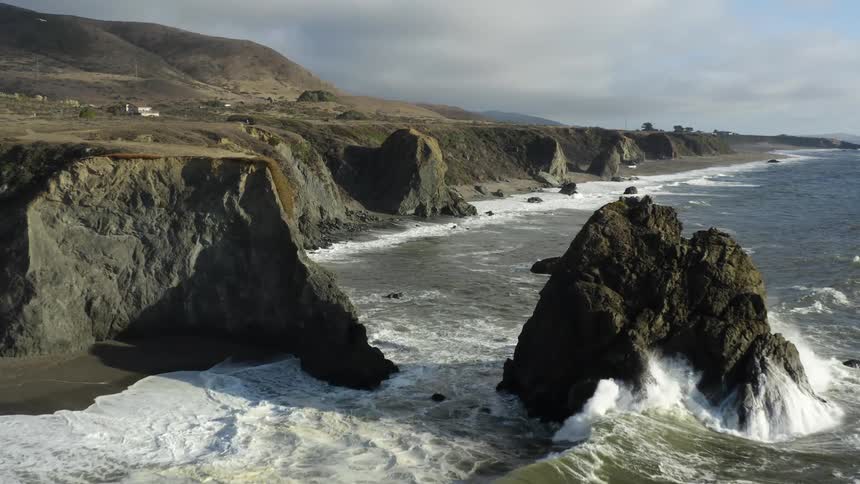 Coastal bluff with waves rolling in and splashing against rock formation on a cloudy day