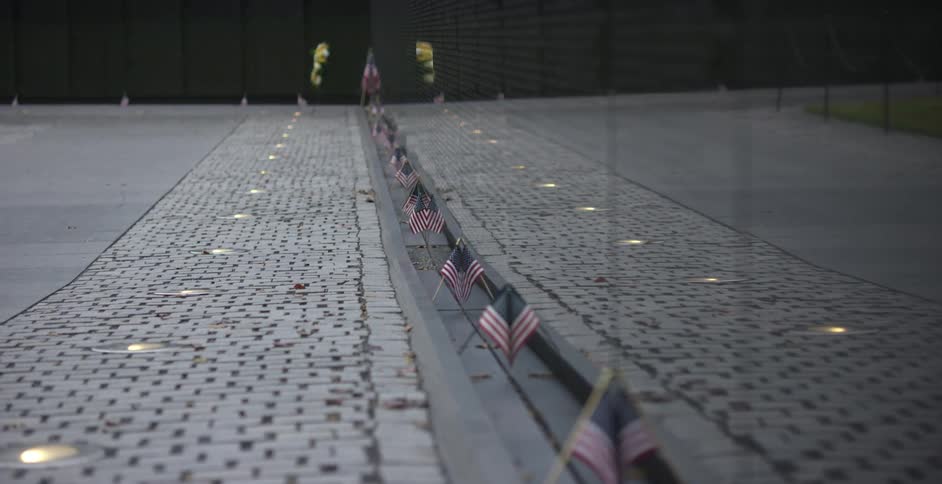 A monument wall in black lined with small american flags with a path and lights outdoors