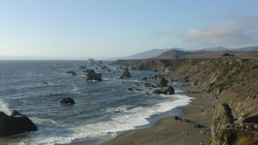 The sun shines on an ocean while its waves lap the shore