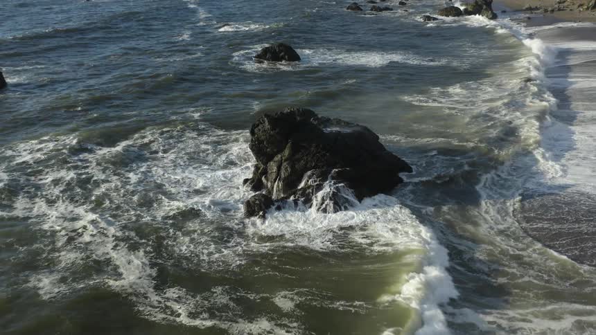 Small tide with sea foam crashing up unto a shore at daytime next to a small rocky ocean side cliff