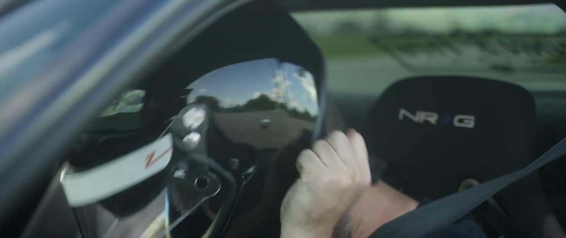 A young man sitting in the drivers seat of a sports car puts on a crash helmet