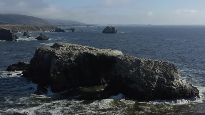 Rocks in the ocean close to a shoreline with cliffs on a sunny day