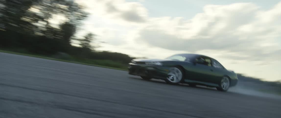 Car drives fast down a road at sunset and makes a sharp turn with trees and power lines in the back ground