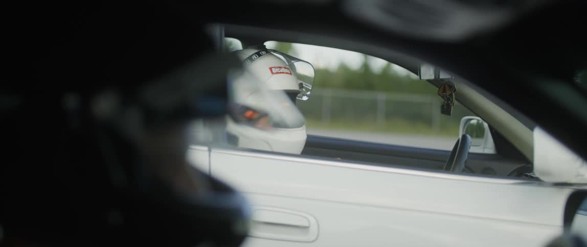 Two race car drivers wearing crash helmets give each other thumbs up from their separate cars